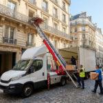 Monte-meubles professionnel déchargeant des cartons vers un balcon dans une rue pavée du quartier Latin à Paris.