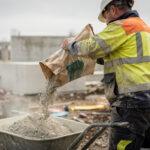 Homme versant du béton depuis un sac de 25 kg dans une brouette sur un chantier extérieur