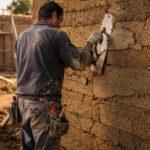 Artisan appliquant un enduit en terre crue sur un mur de pisé